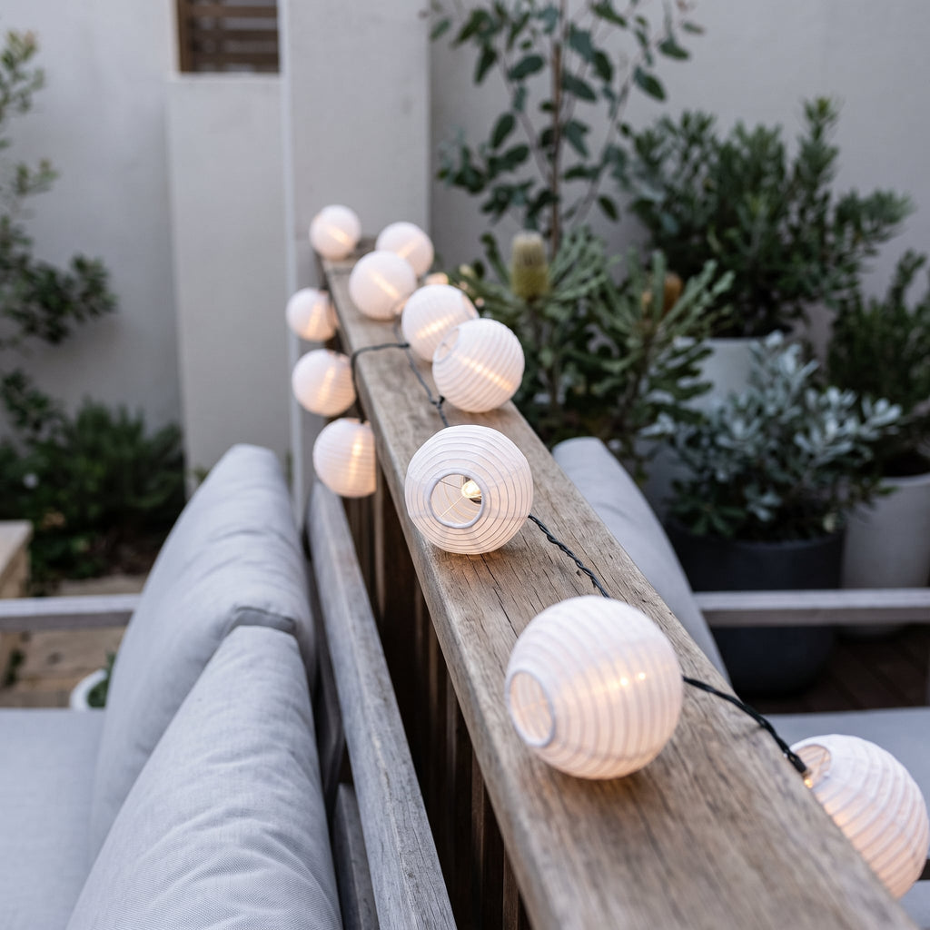 White solar lantern string lights glowing on a courtyard railing at dusk